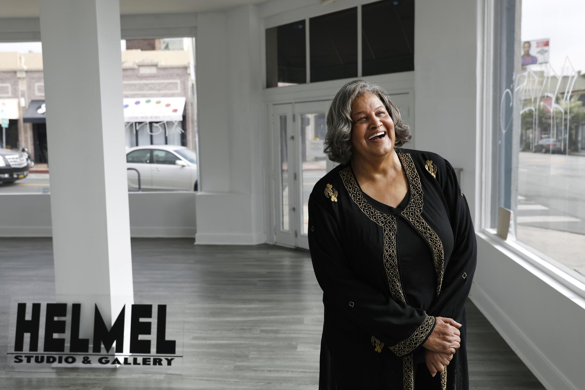 A woman with gray hair and a black dress laughs inside an empty art studio
