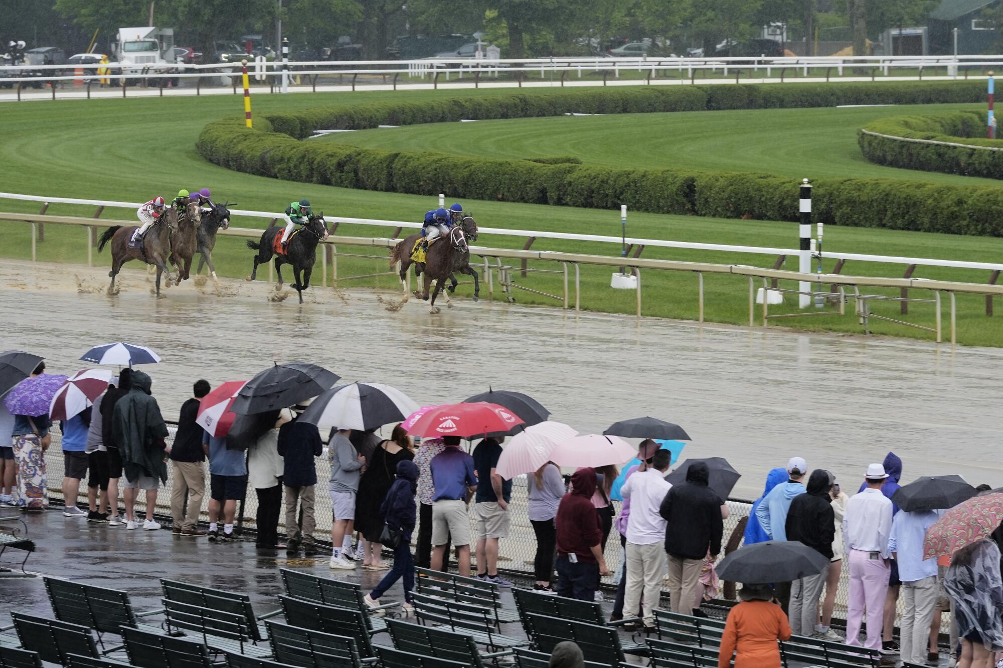 Horse racing fans watch in a steady drizzle as thoroughbreds race on a wet track during Saratoga Race Course on Saturday.