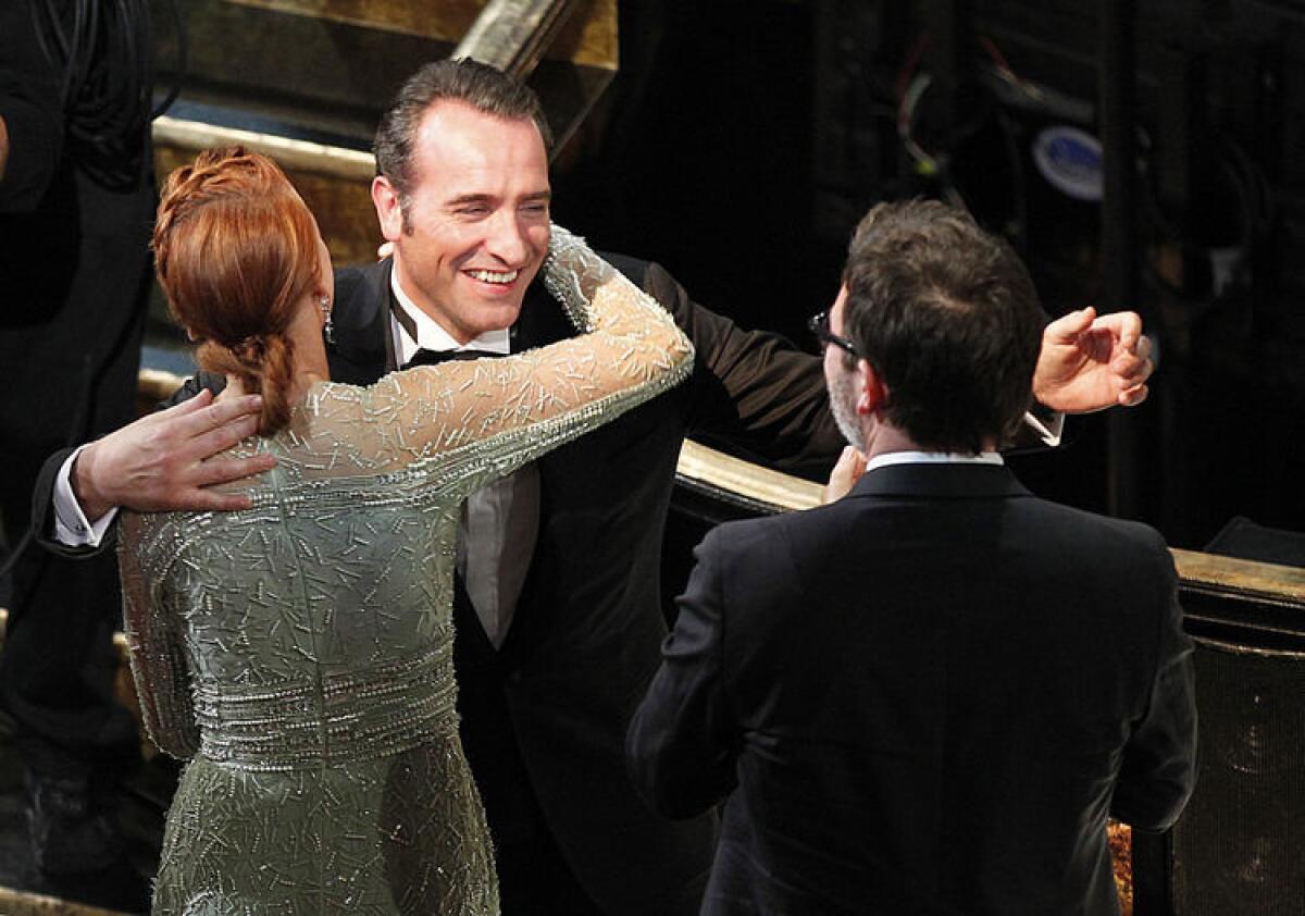 Jean Dujardin hugs Berenice Bejo and "The" Artist director Michel Hazanavicius, right, after winning the Oscar for Best Actor at the 84th Annual Academy Awards show. The black and white film also won in the picture, director, costume design and original score categories.