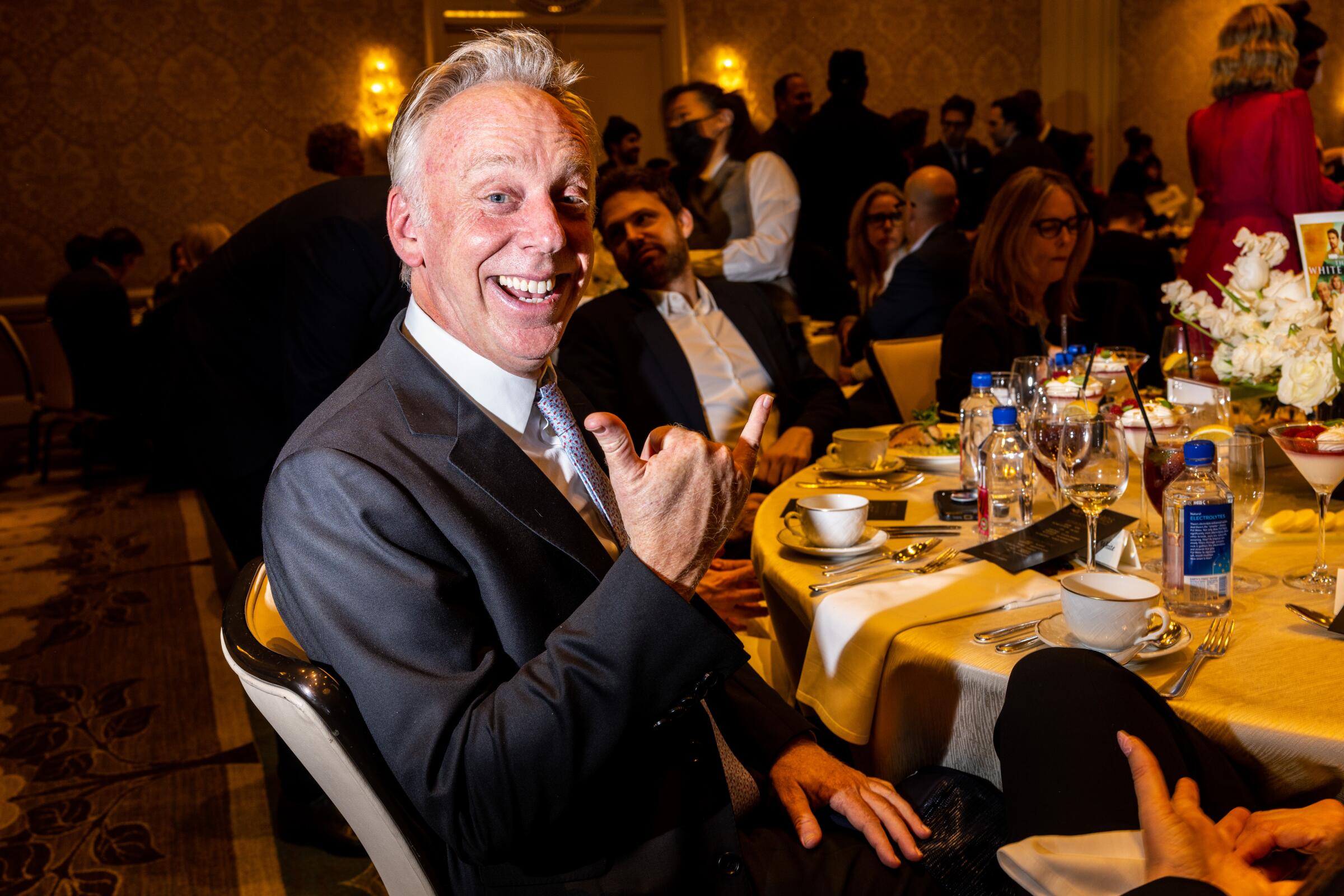 Mike White wears a suit and flashes a thumbs up while at a dinner event.