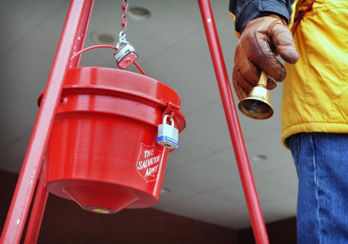 A Salvation Army donation kettle and the hand of someone ringing a bell.