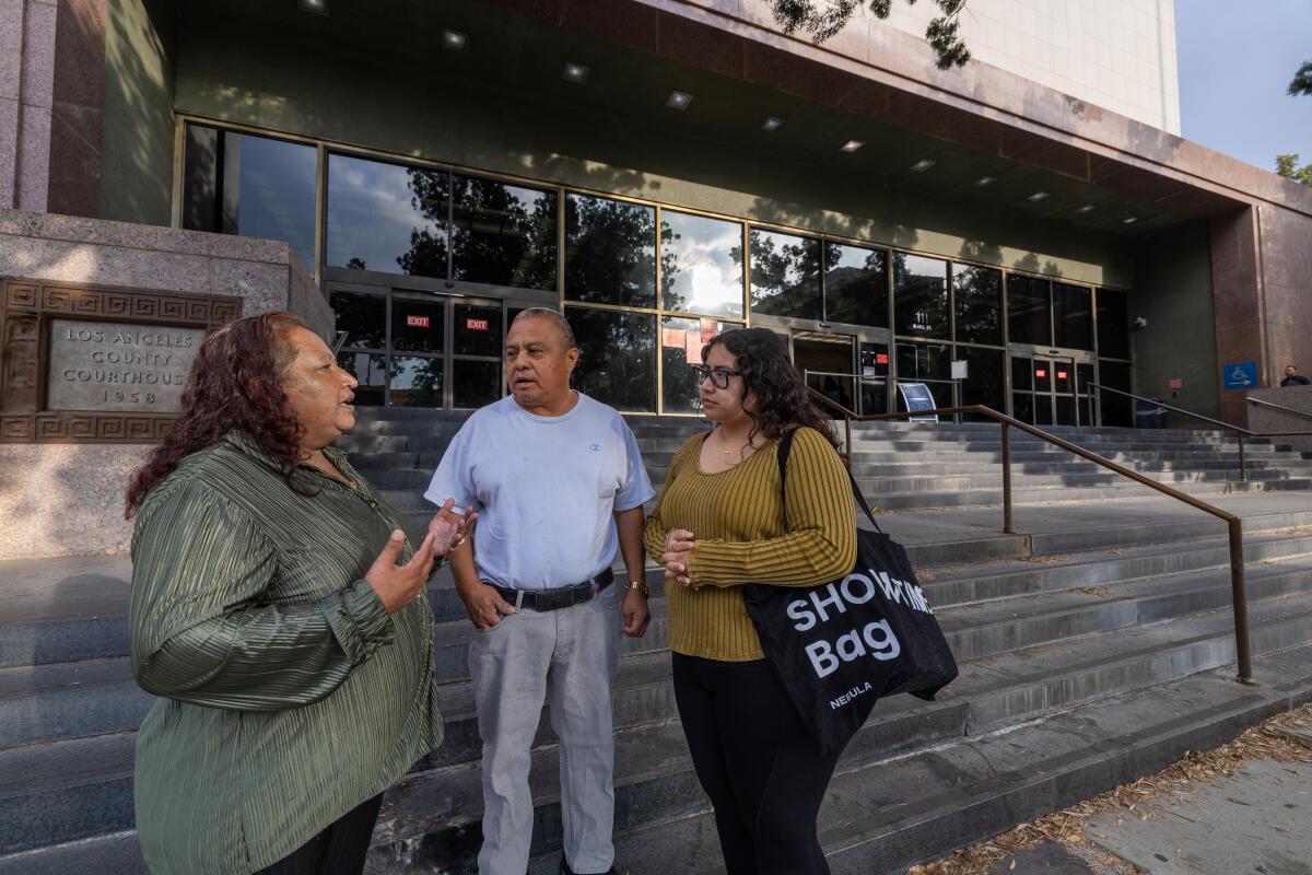 Three people talk in front of a building.