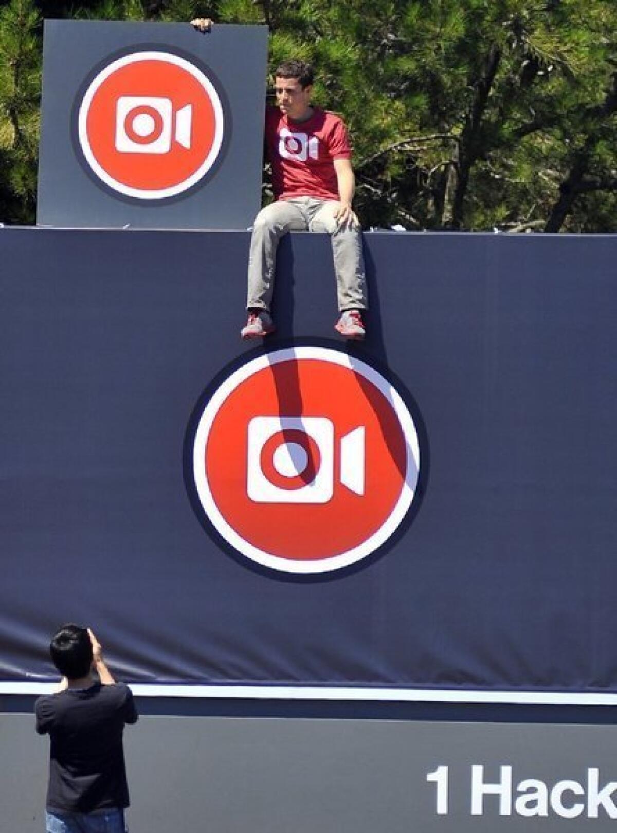 Instagram engineer Ryan Gomba sits on top of the Facebook sign at Facebook's headquarters in Menlo Park, Calif., after a media event announcing Instagram video.