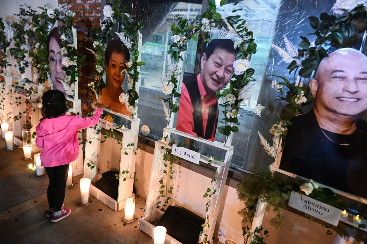 A girl lays a flower in front of a row of portraits and candles