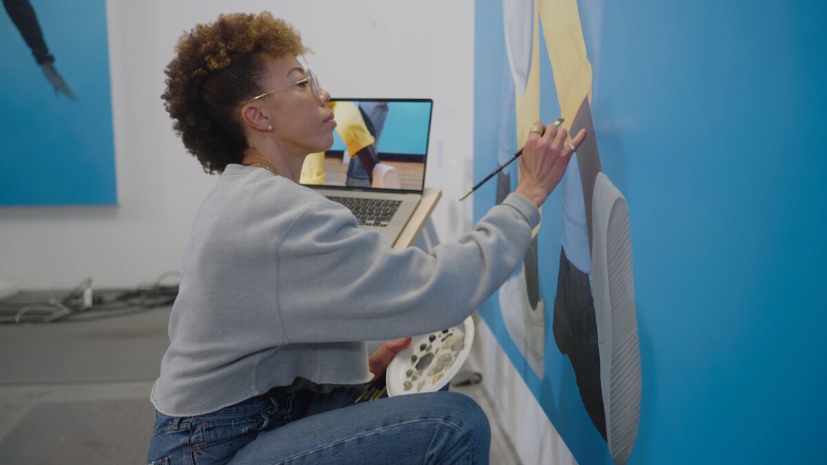 a woman in all blue paints on a wall with an open laptop next to her