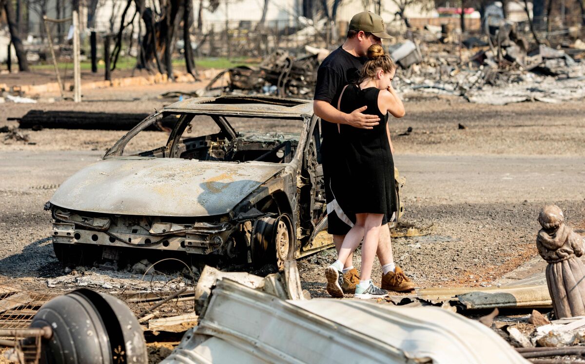 Two people hug while surrounded by ruins of a home destroyed by fire