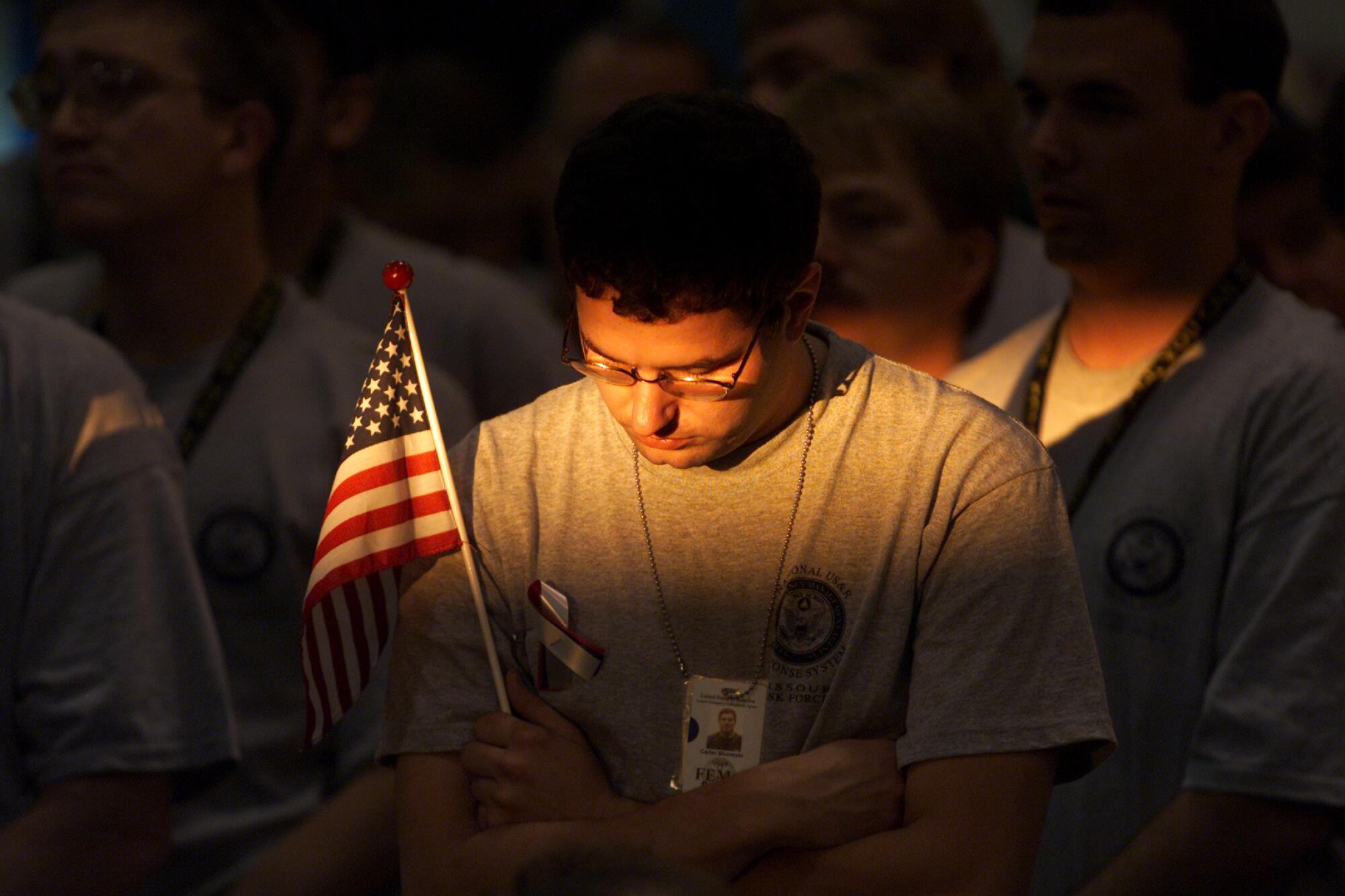 A man holds a small U.S. flag and bows his head