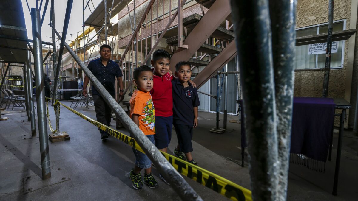 Brothers, Mathew Rosales, 3, left, Emiliano, 5, and Rudy Jr., 7, accompanied by their father Rudy Rosales, 34, pass between scaffolds in the court yard of Marmion Royal apartments in Highland Park.