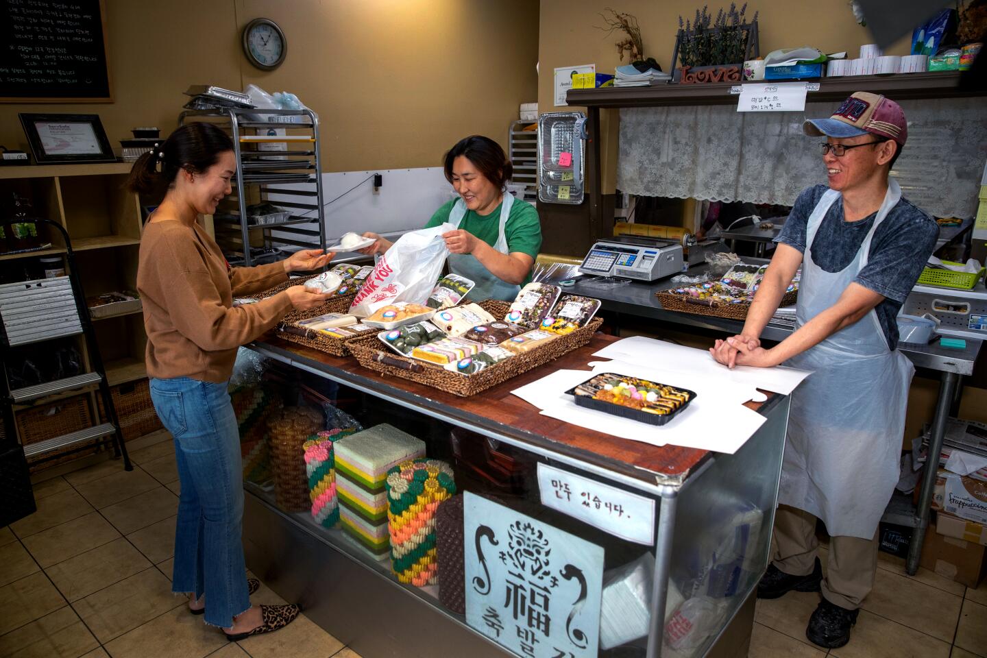 From behind the counter, Lim Bang An owners Yoon Here Nam, left, and Phillip Nam sell fresh tteok to Elena Hahm of Irvine.
