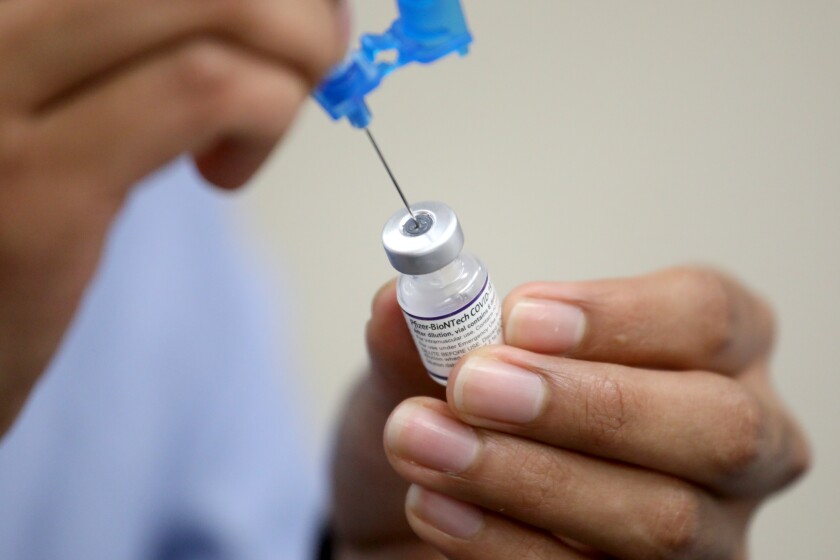 یک داروساز سرنگی را با واکسن کووید-۱۹ Pfizer-BioNTech آماده می‌کند. 