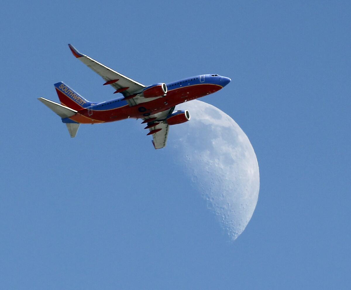 A jet crosses over a crescent moon during a daytime flight. 