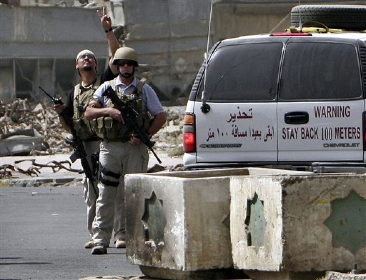 FILE - In this Tuesday, July. 5, 2005, file photo, a private contractor gestures to their colleagues flying over in a helicopter as they secure the scene of a roadside bomb attack in Baghdad, Iraq. (AP Photo/Khalid Mohammed, File)