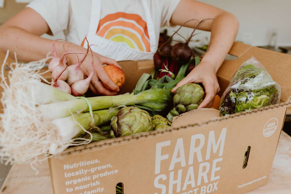 Hands reach into a farm share box from the Ecology Center filled with vegetables.