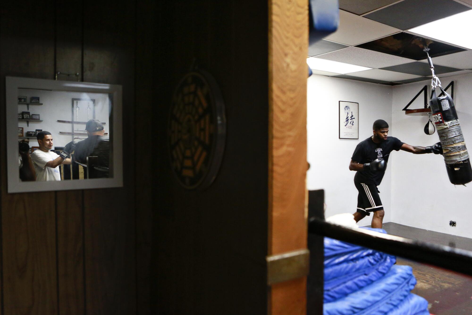 A man in workout gear and boxing gloves hits the heavy bag inside a gym.