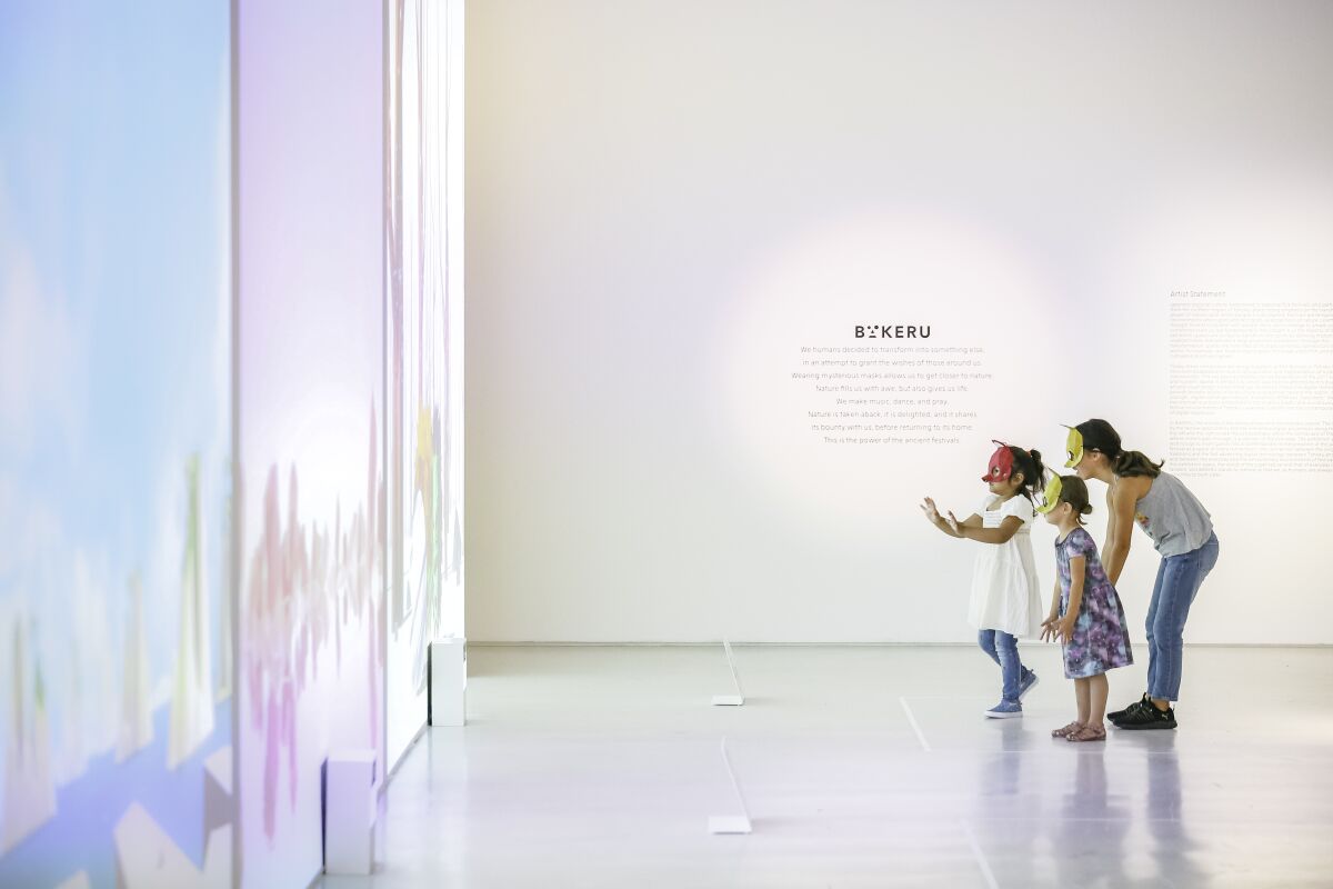 Visitors don masks for the interactive exhibition, "Bakeru: Transforming Spirits," at Japan House Los Angeles.