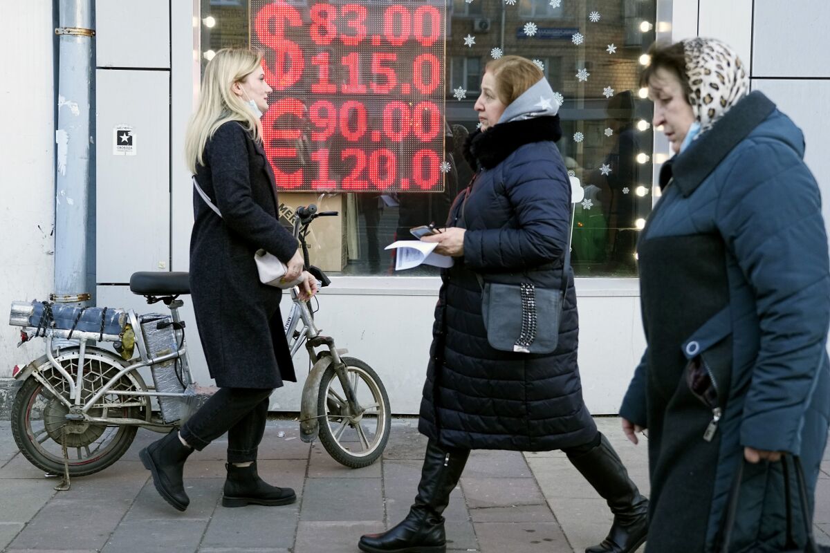FILE - People walk past a currency exchange office screen displaying the exchange rates of U.S. Dollar and Euro to Russian Rubles in Moscow, on Feb. 28, 2022. The U.S. Treasury Department will not allow any dollar debt payments to be made from Russian government accounts at U.S. financial institutions, an agency spokesperson said Tuesday morning. (AP Photo/Pavel Golovkin, File)