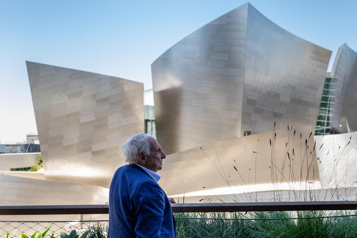 A man in a blue suit stands in an outdoor lounge near Walt Disney Concert Hall