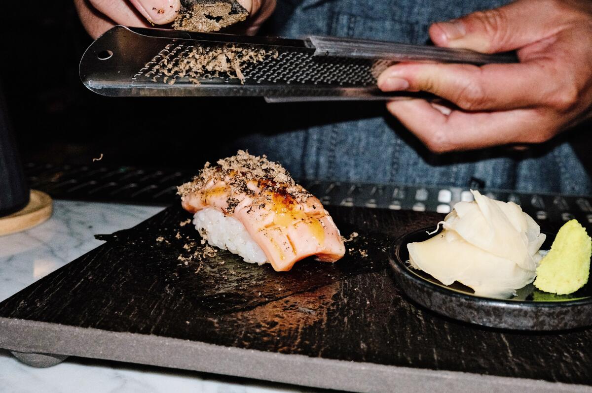 A hand shaves black truffle onto salmon and rice at Iki Nori sushi bar in Hollywood.