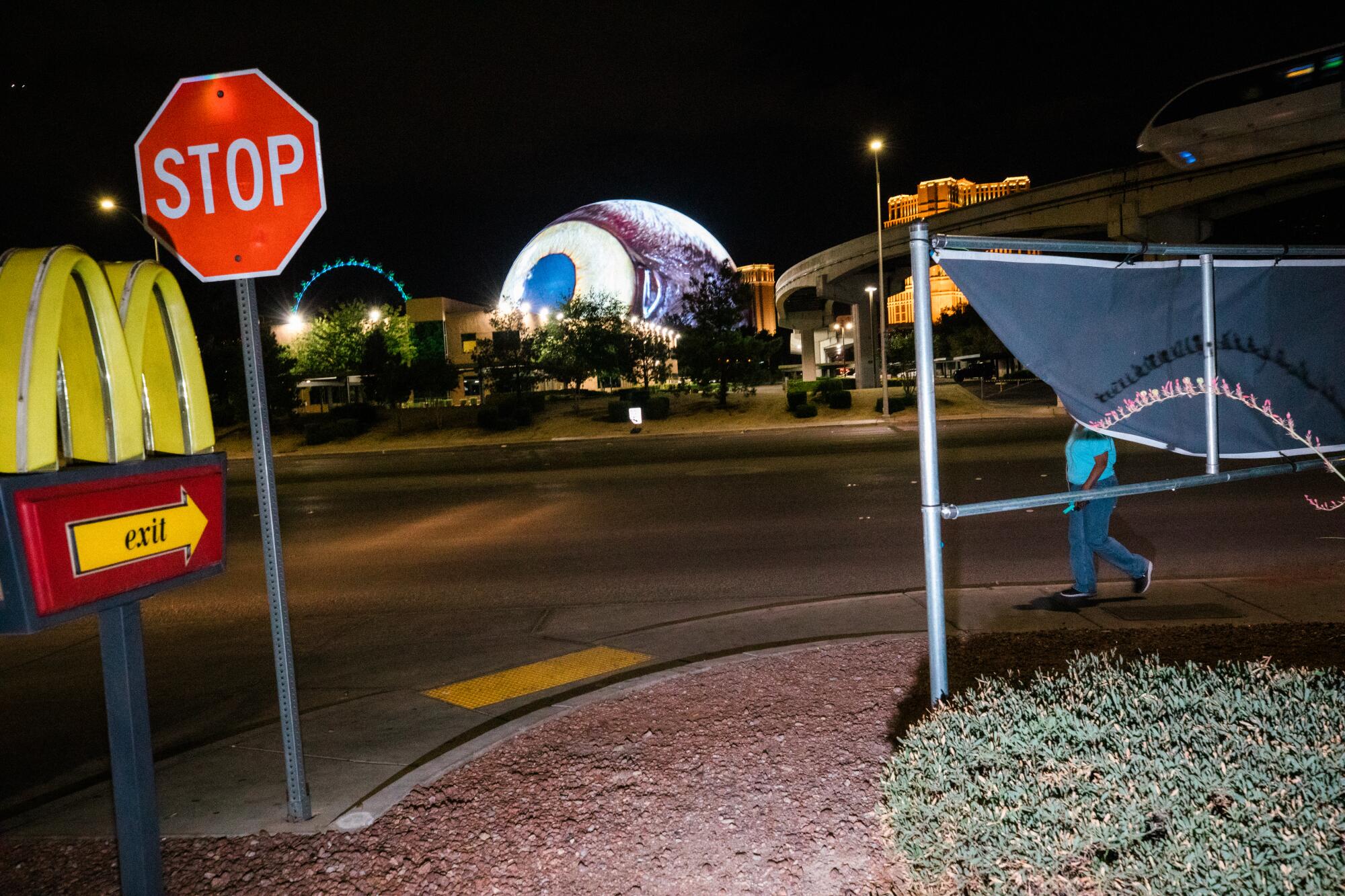 A spherical building broadcasting the image of an eye is seen from a McDonald's drive-thru.