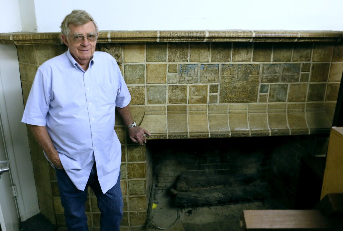 Alan Batchelder, during a 2018 visit to a building owned by La Cañada Unified School District, poses with a fireplace made in 1923 by his grandfather, Arts and Crafts tile artist Ernest Allan Batchelder.
