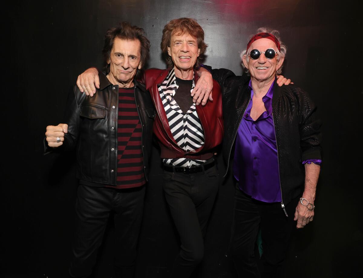 Ronnie Wood, left, Mick Jagger and Keith Richards smile and stand with arms around one another's shoulders.