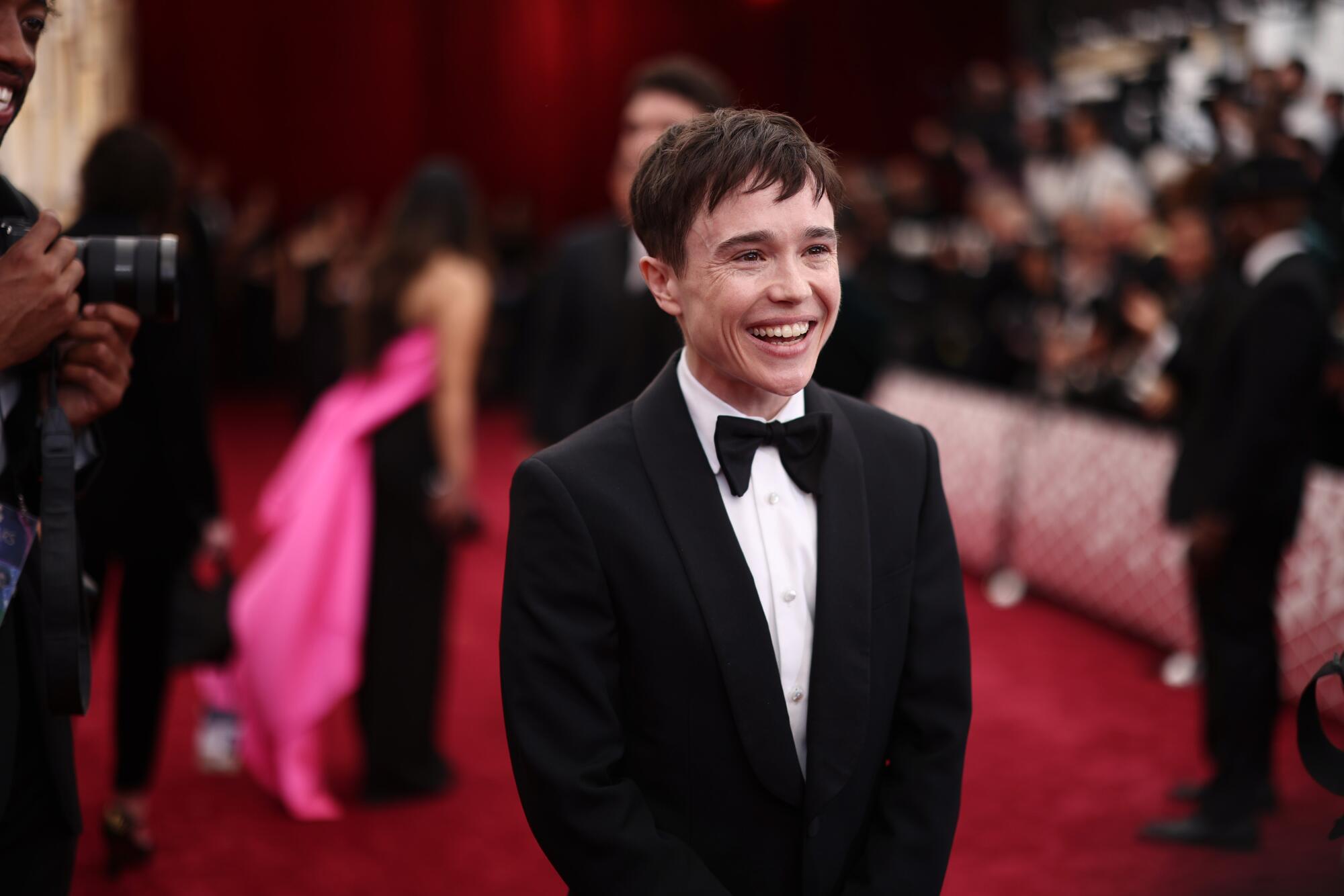 Elliot Page in a tuxedo smiles on a red carpet