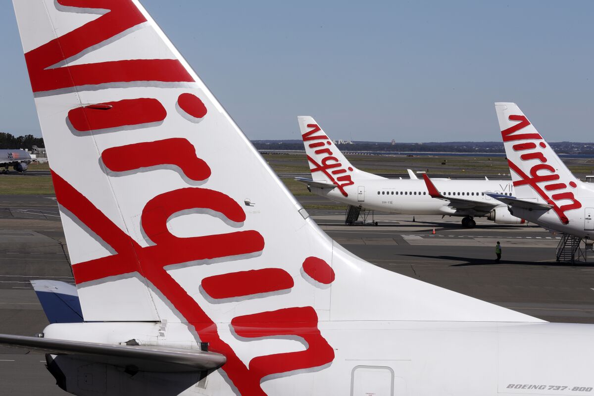 Virgin Australia planes are parked at terminal at Sydney Airport in Sydney, Wednesday, Aug. 5, 2020. Virgin Australia will cut about 3000 jobs as the airline struggles with the effects of the coronavirus pandemic. (AP Photo/Rick Rycroft)