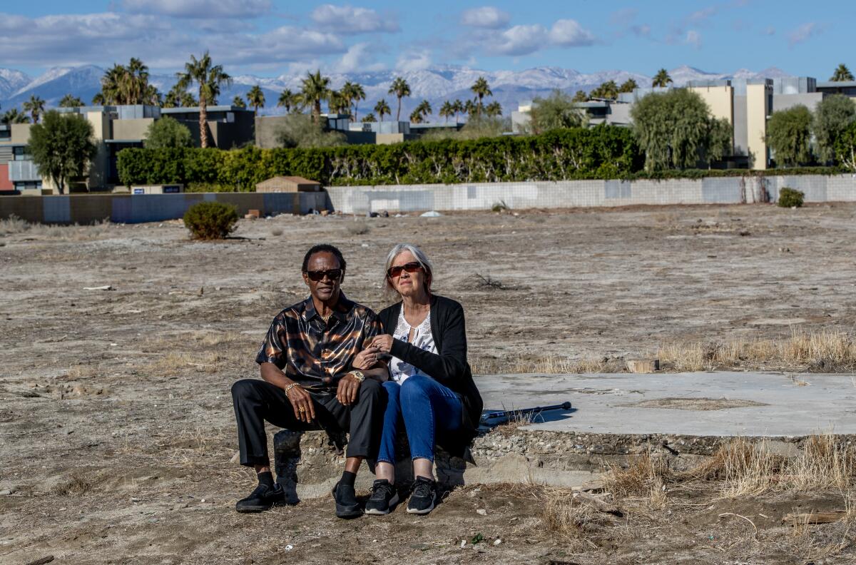 A man and woman sit on a concrete slab in an undeveloped area.