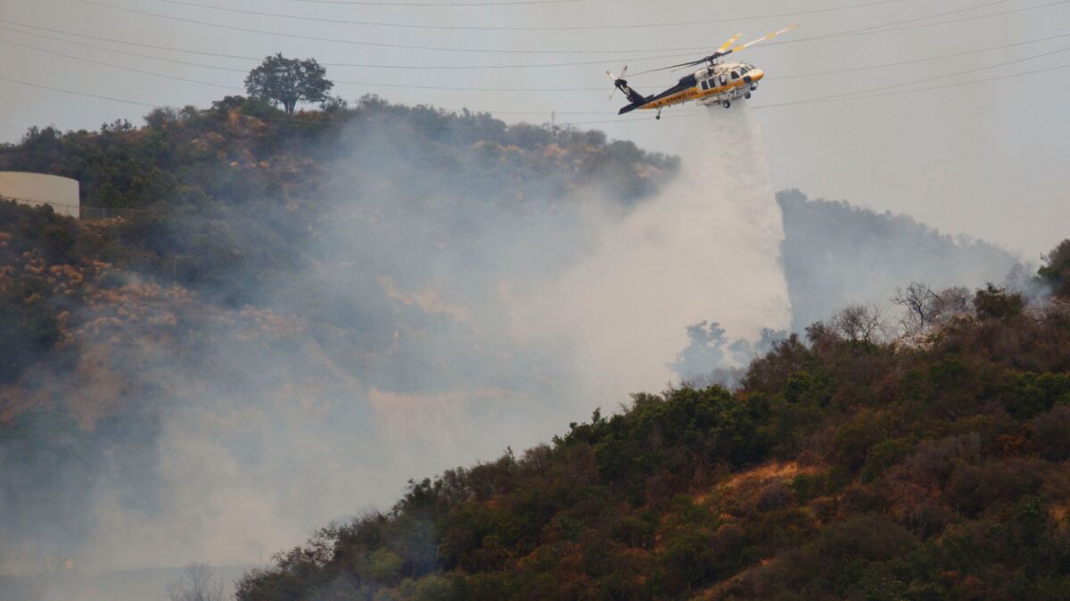 An L.A. County firefighting helicopter makes a drop as crews battle a brush fire in Mandeville Canyon on Sunday.