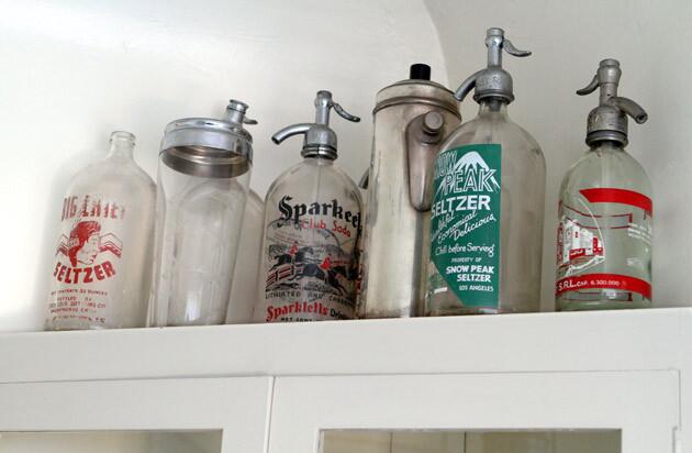 The hutch's shelves hold a collection of seltzer bottles.