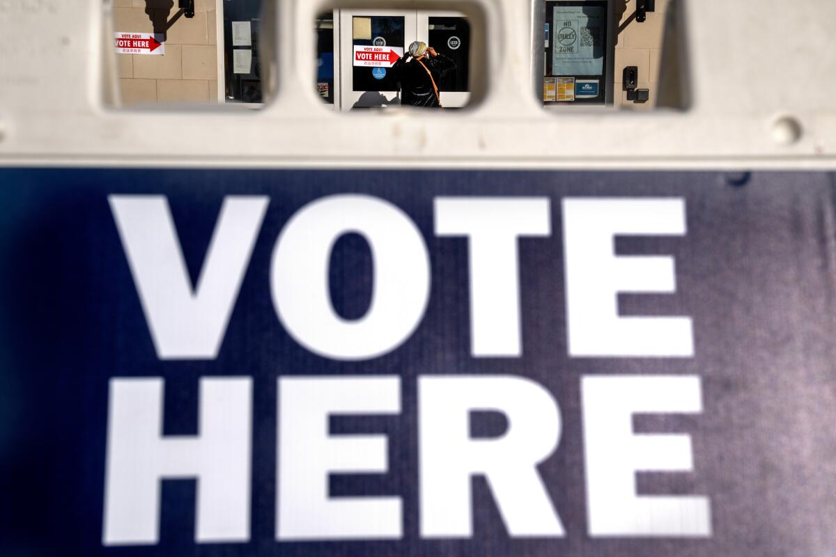 ARCHIVO - A través de un cartel "vota aquí", se observa a una mujer mientras entra en un colegio electoral
