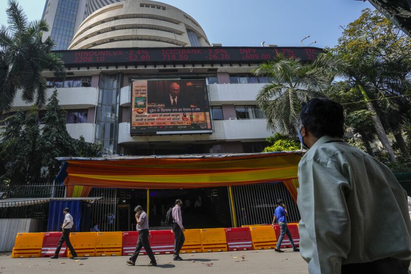A man watches a screen showing a news item featuring Russian President Vladimir Putin on the facade of the Bombay Stock Exchange (BSE) building in Mumbai, India, Thursday, Feb. 24, 2022. Just what a vulnerable world economy didn’t need — a conflict that accelerates inflation, rattles markets and portends trouble for everyone from European consumers to indebted Chinese developers and families in Africa that are enduring soaring food prices. Russia’s attack on Ukraine and retaliatory sanctions from the West may not portend another global recession. (AP Photo/Rafiq Maqbool)