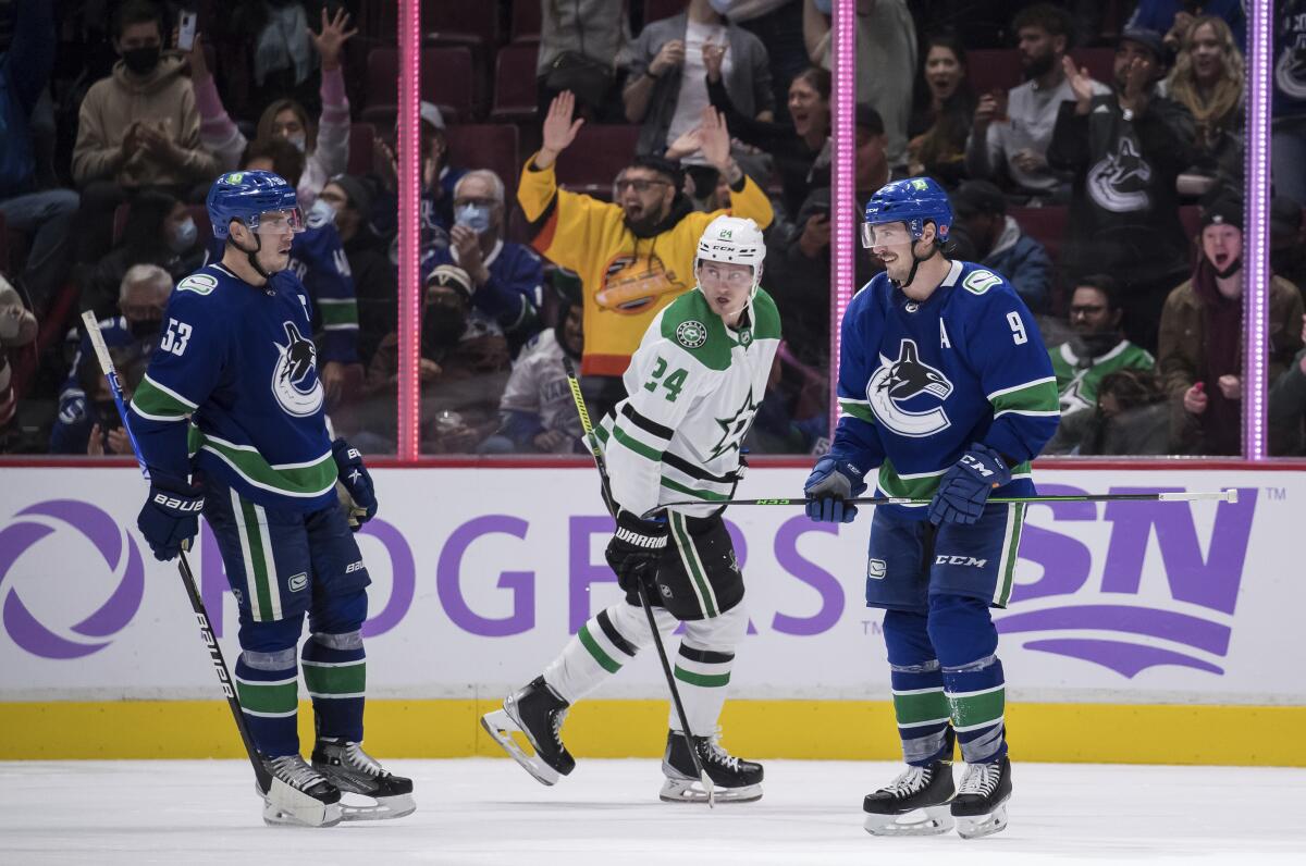 Vancouver Canucks' J.T. Miller (9) and Bo Horvat (53) celebrate Miller's second goal as Dallas Stars' Roope Hintz, of Finland, skates past them during the third period of an NHL hockey game in Vancouver, British Columbia, Sunday, Nov. 7, 2021. (Darryl Dyck/The Canadian Press via AP)