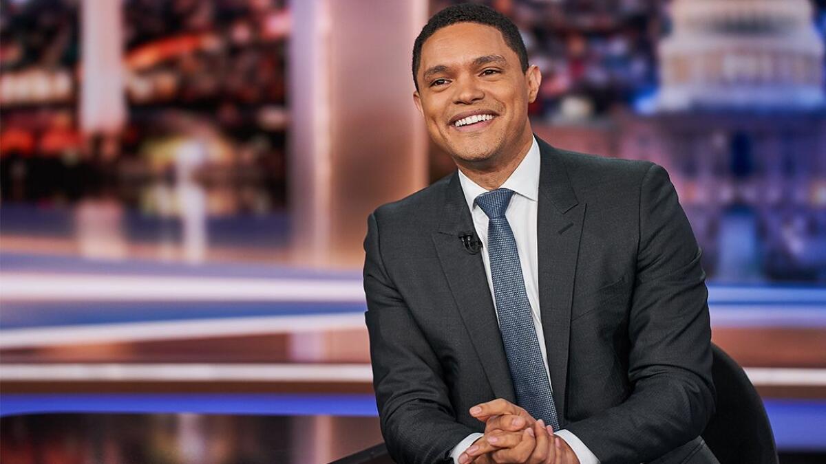 "Daily Show" host Trevor Noah, wearing a suit and tie, is pictured smiling on set