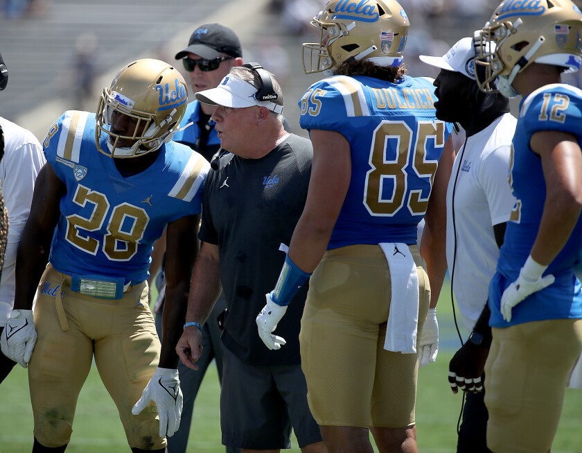 Bruins football coach Chip Kelly talks with players on the sideline.