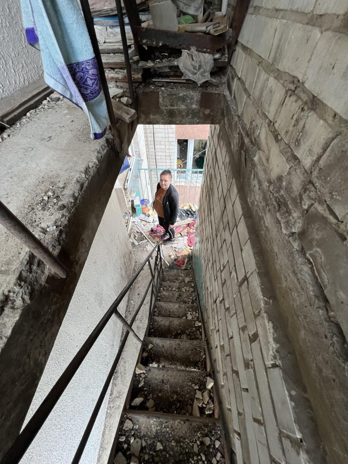 A woman stands in the stairwell of a destroyed building.