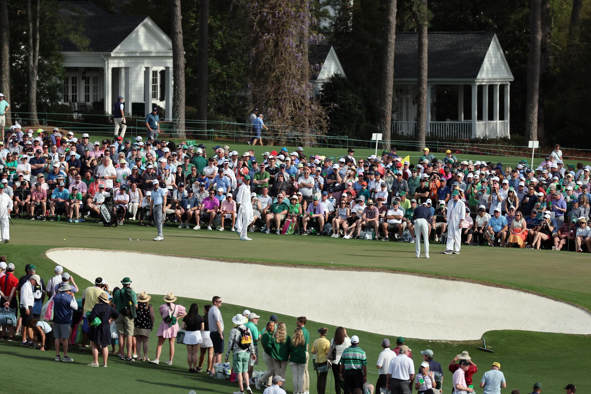 Golfers stand on the green as a large crowd looks on