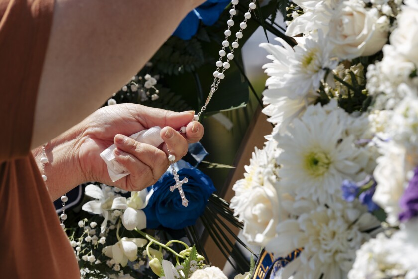 An El Monte resident hangs a rosary on one of the many flower wreaths at a growing memorial for two El Monte police officers.