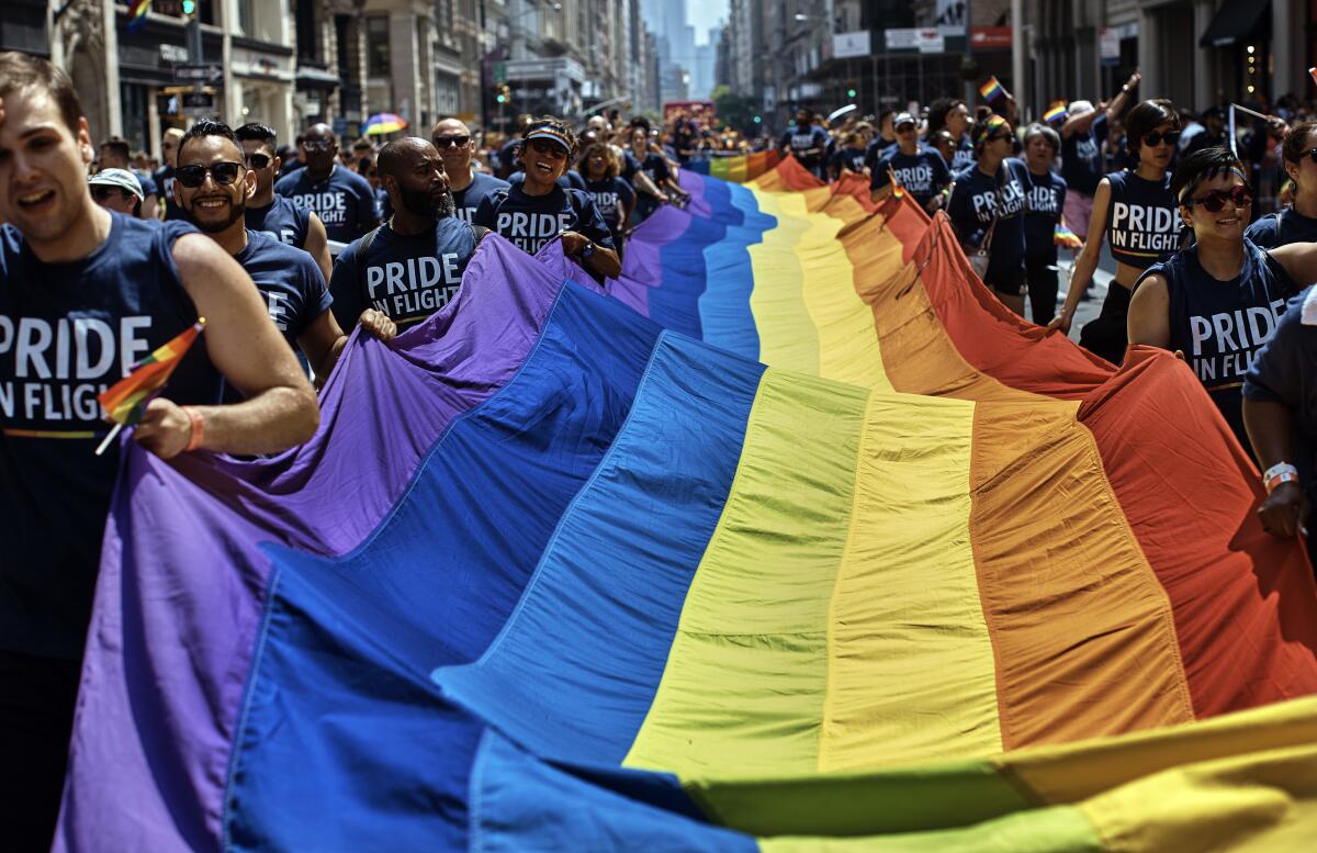 Pride parade marchers carrying large rainbow flag 