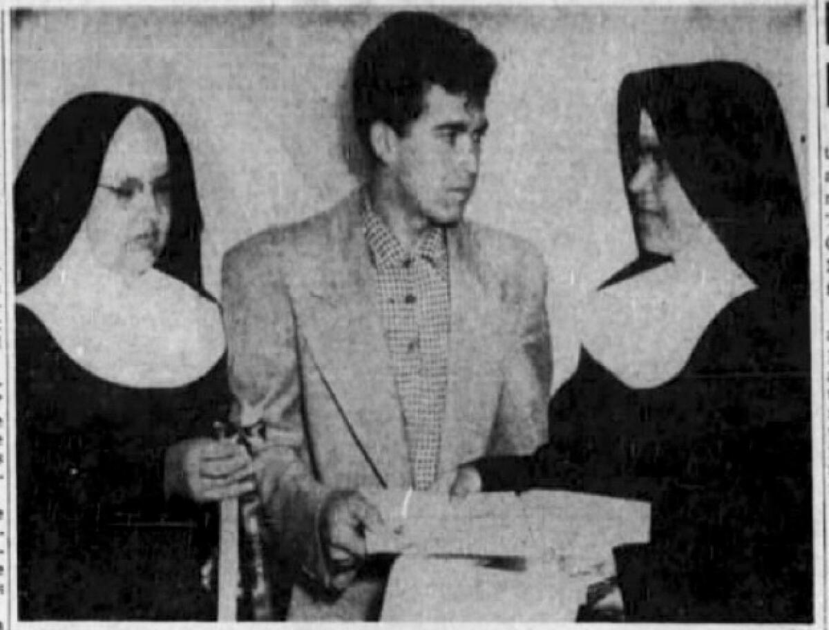 A young man with dark hair, wearing a jacket and holding documents, flanked by two nuns