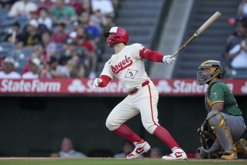 Taylor Ward (3), de los Angelinos de Los ?ngeles, batea cuadrangular mientras el receptor de los Atléticos de Oakland, Shea Langeliers, observa durante la primera entradad el juego de béisbol del lunes 24 de junio de 2024, en Anaheim California. (AP Foto/Eric Thayer)