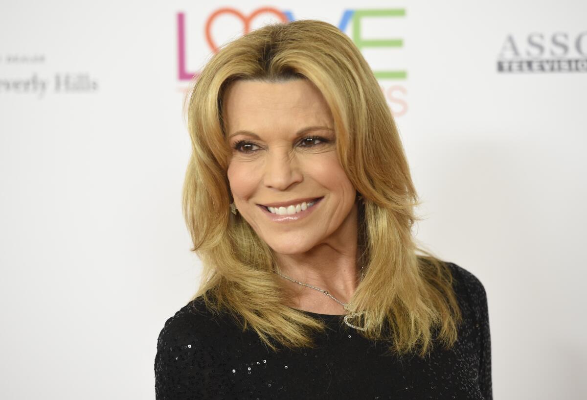 Vanna White smiles in a black outfit while looking over her shoulder and leaning slightly forward