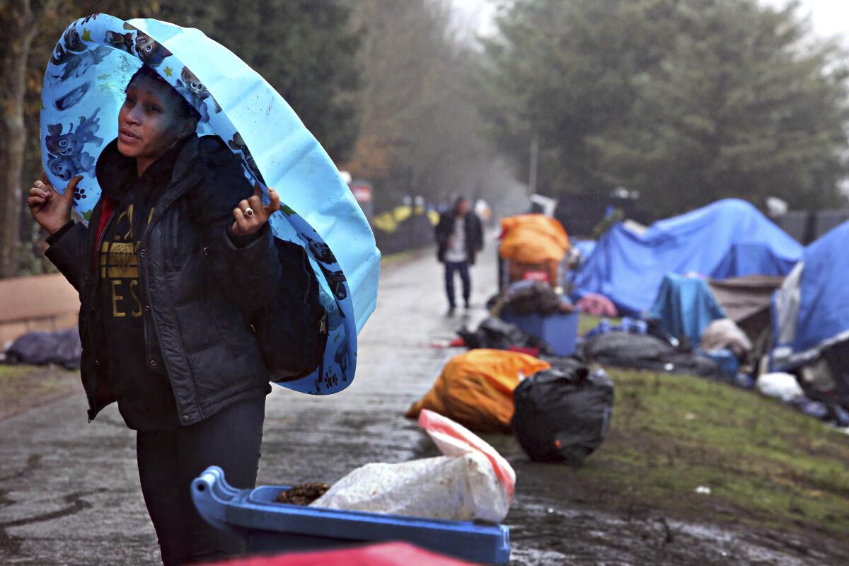A person with a plastic wading pool over their head stands next to a homeless encampment