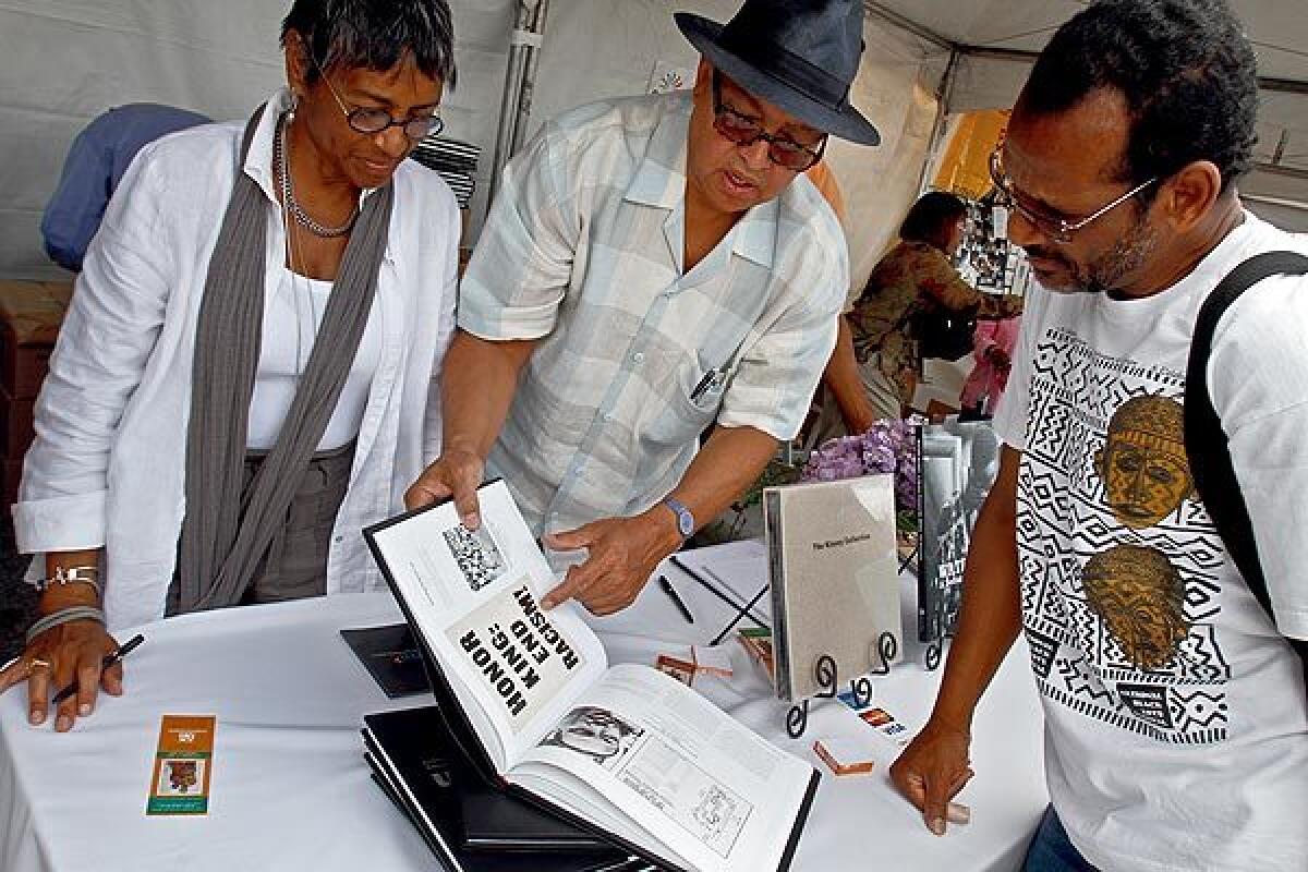 A woman and two men look at a book at the Leimert Park Book Fair, returning Saturday.