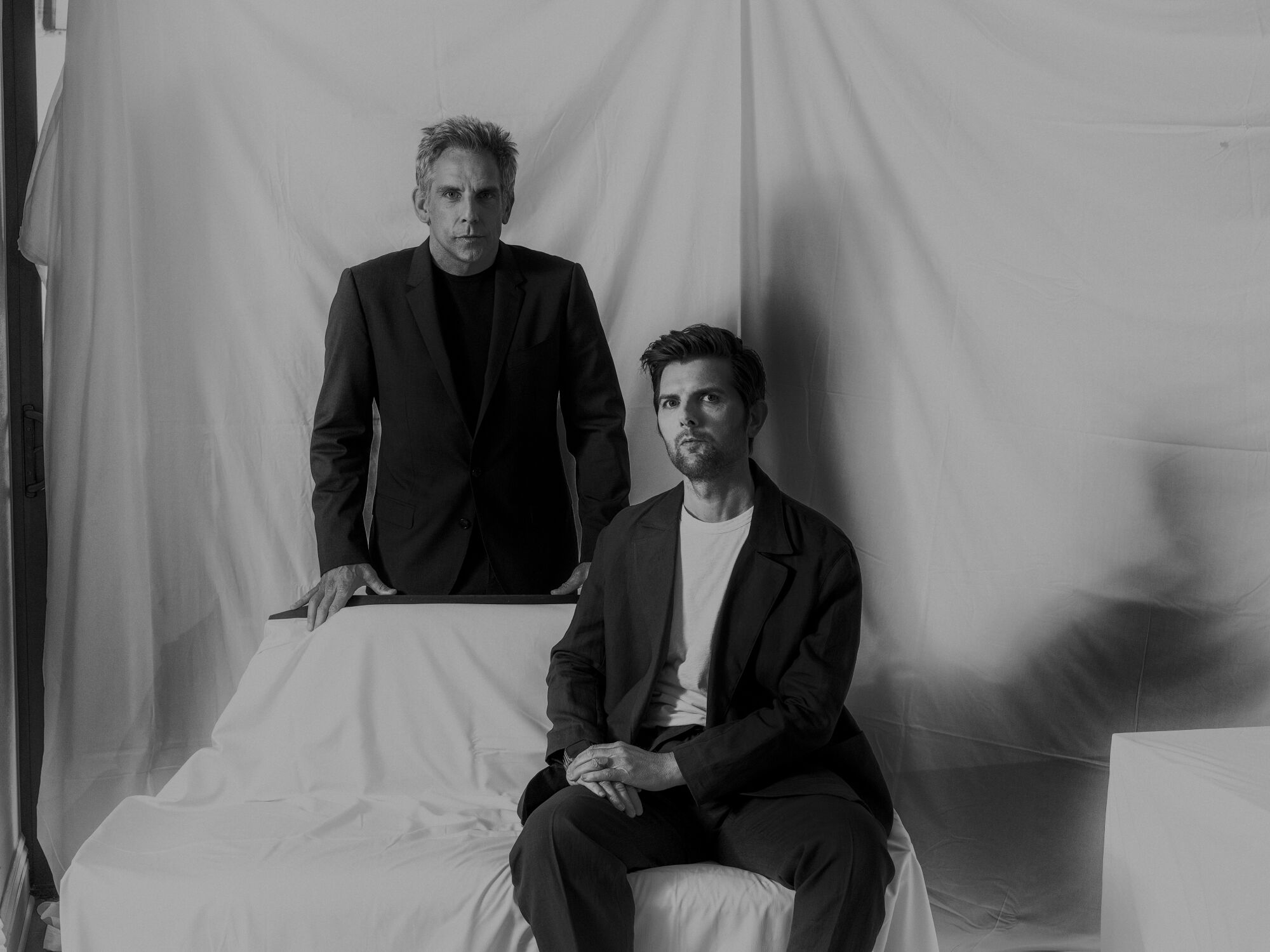 Two men pose for a portrait in front of a white fabric background