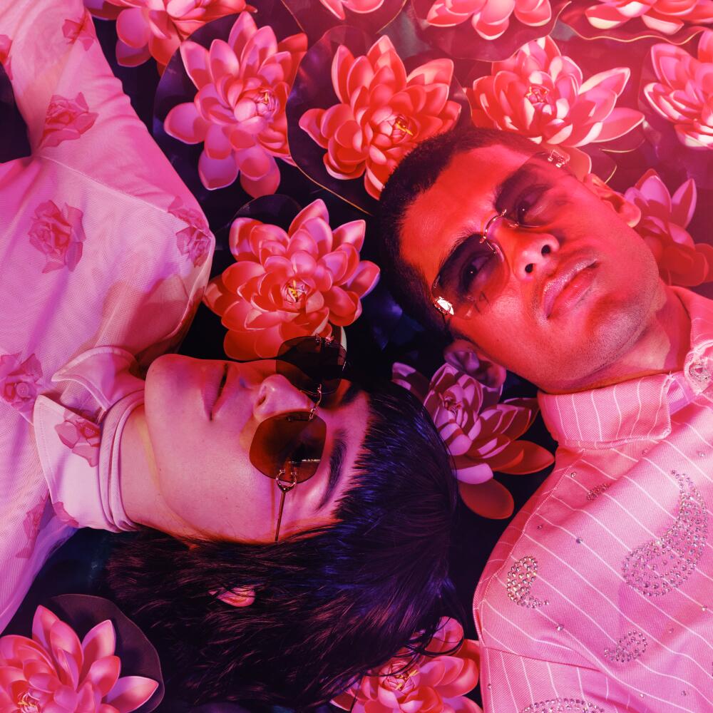 Two people lay in a field of fake pink flowers.