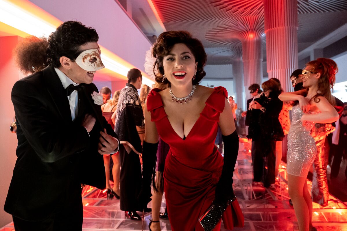 A masked man in a tuxedo and a woman in a red evening gown and jewels at a party in a scene from "House of Gucci."