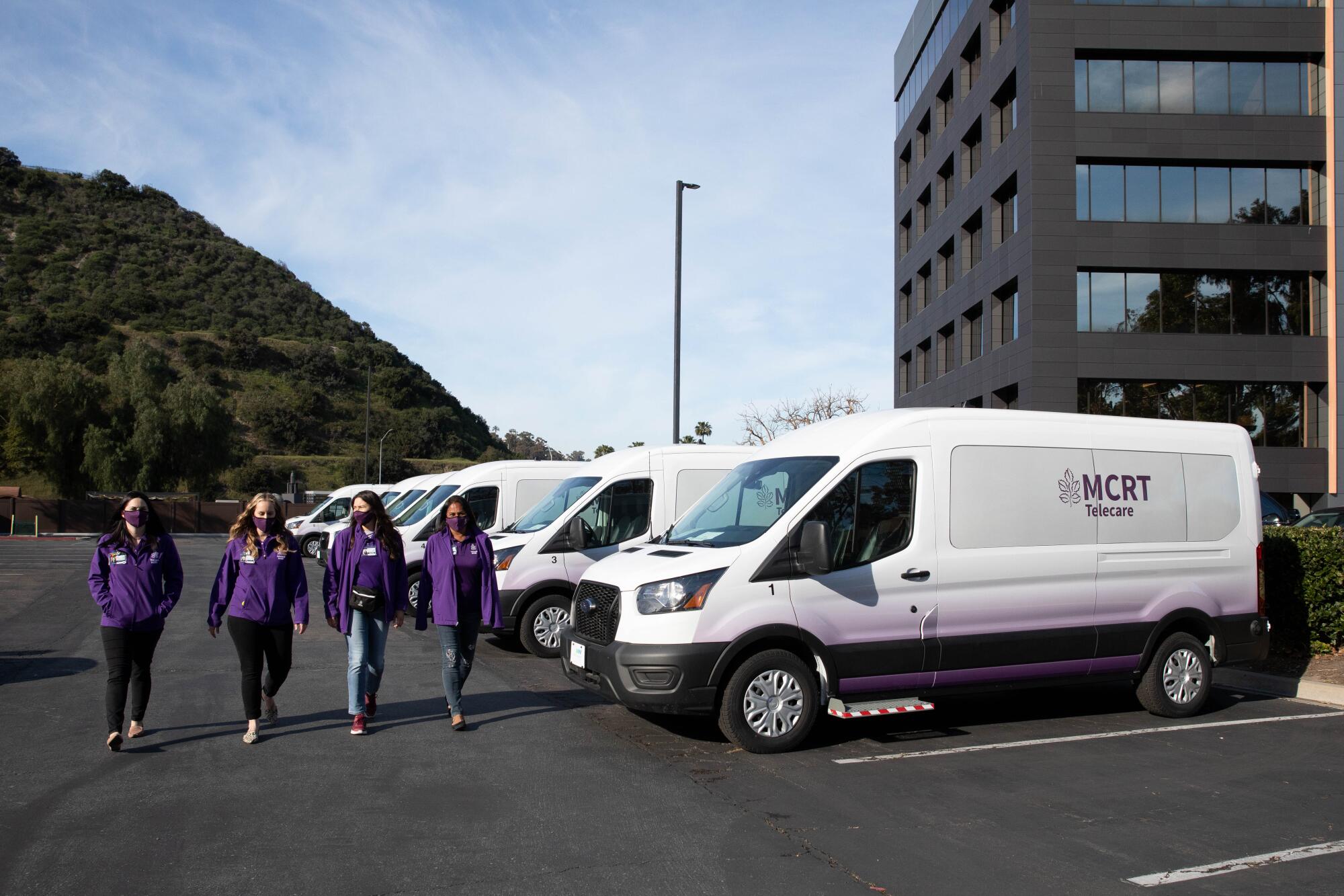 Four people in purple shirts walk near several white vans.