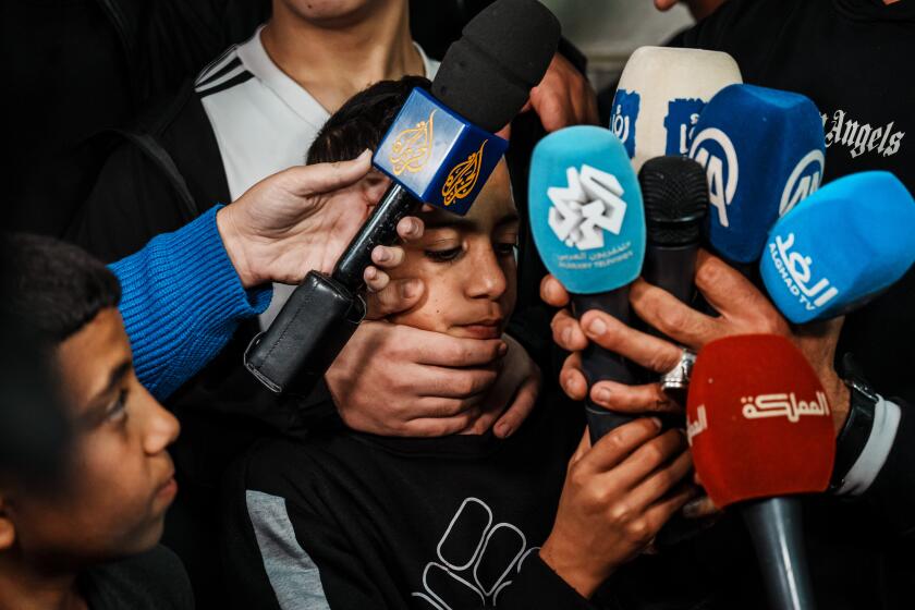 RAS AL A'MUD, ISRAEL -- NOVEMBER 28, 2023: Ayham Salaymah holds up up microphones as his father Nawaf speaks to reporters after the his brother Ahmad Salaymah, 14, release from prison, in their home in Ras Al A'Mud, Israel, Tuesday, Nov. 28, 2023. When Israel agreed with Hamas to a prisoner swap, it published a list of 300 Palestinians it considered for released, the majority of them children. It's a reflection of an incarceration system, Palestinians and rights groups say, that targets children as enemy combatants, elevating offenses like rock throwing into security-related violations that carry a years-long sentence. (MARCUS YAM / LOS ANGELES TIMES)
