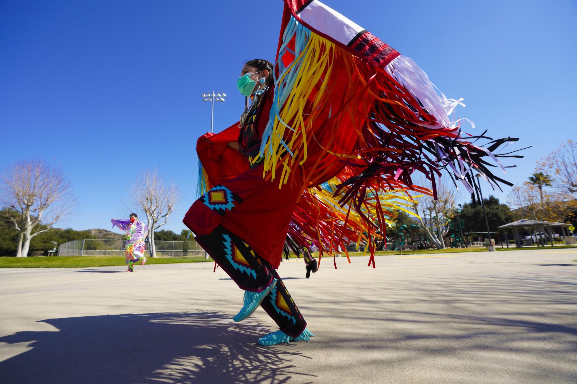 A woman dances in a multicolored Indigenous fringed dance costume.